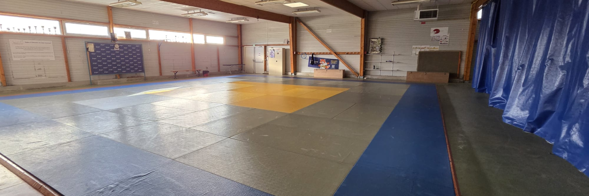 Salle de gym avec tatamis, tableau et rideau.