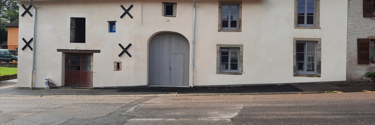 Maison à deux étages avec toits en tuiles rouges, portes et fenêtres marquées d'une croix noire.