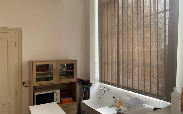 Cuisinette avec évier, micro-ondes, étagère, rideau et produits de nettoyage.