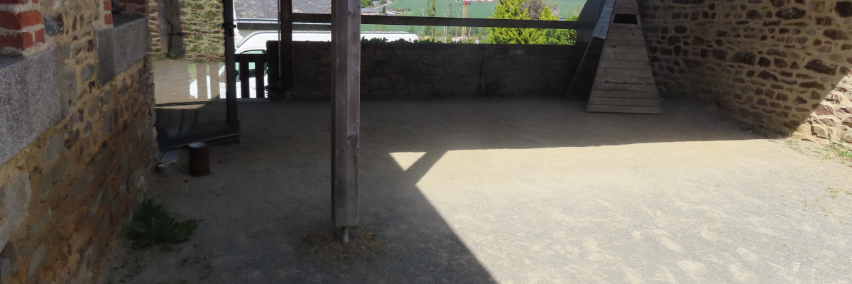 Terrasse en béton avec vue sur paysage, murs en pierre et brique, toit en bois.