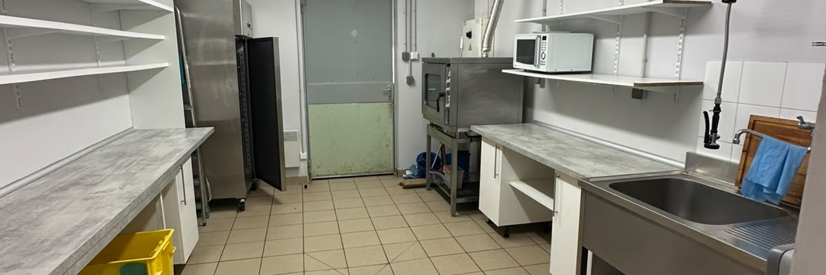 Cuisine avec plans de travail, étagères, évier, frigo, et lumières fluorescentes.