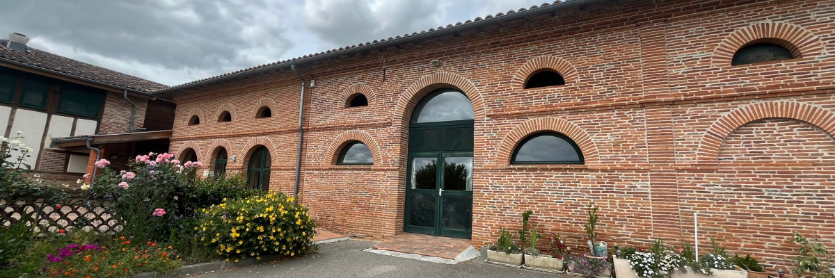Bâtiment en brique avec arches, fleurs et parking.