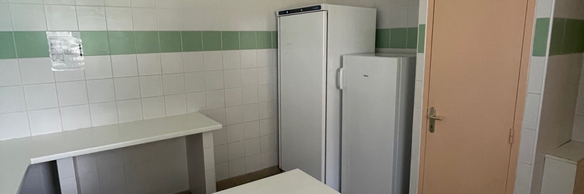 Cuisine avec frigo, table, chaises, évier et porte.