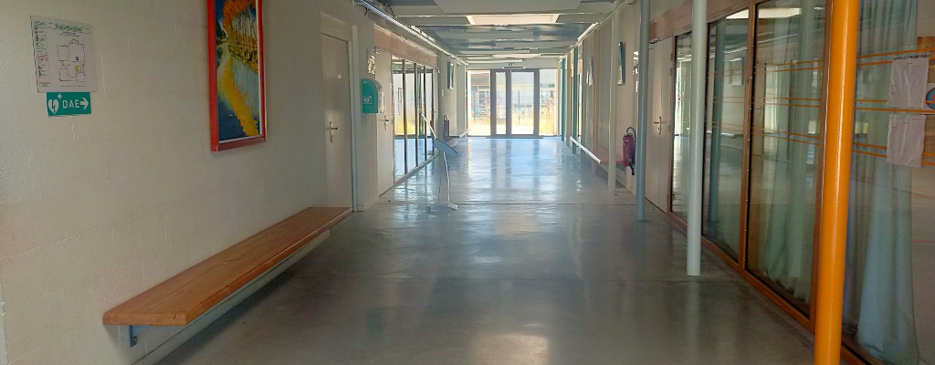 Couloir avec banc, tableaux, portes vitrées et défibrillateur.