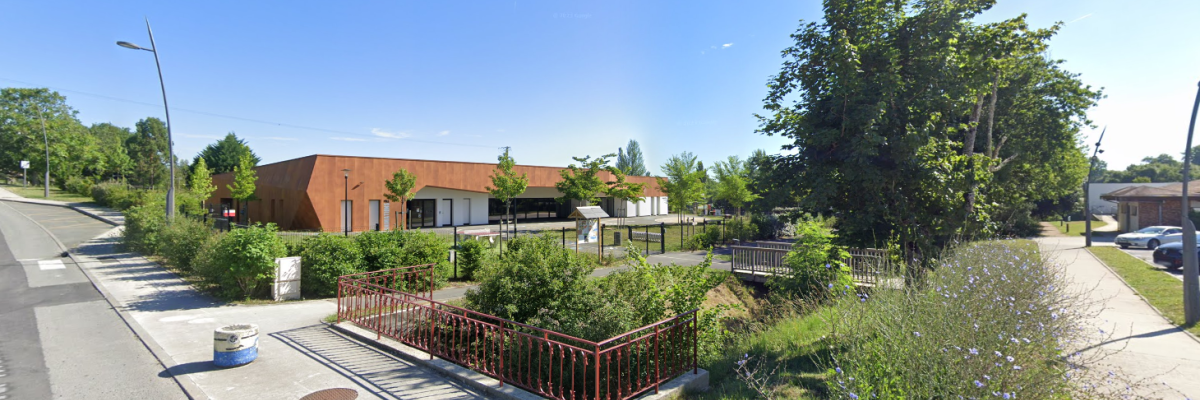 Bâtiment avec toits plats, arbres, buissons, clôture et route.