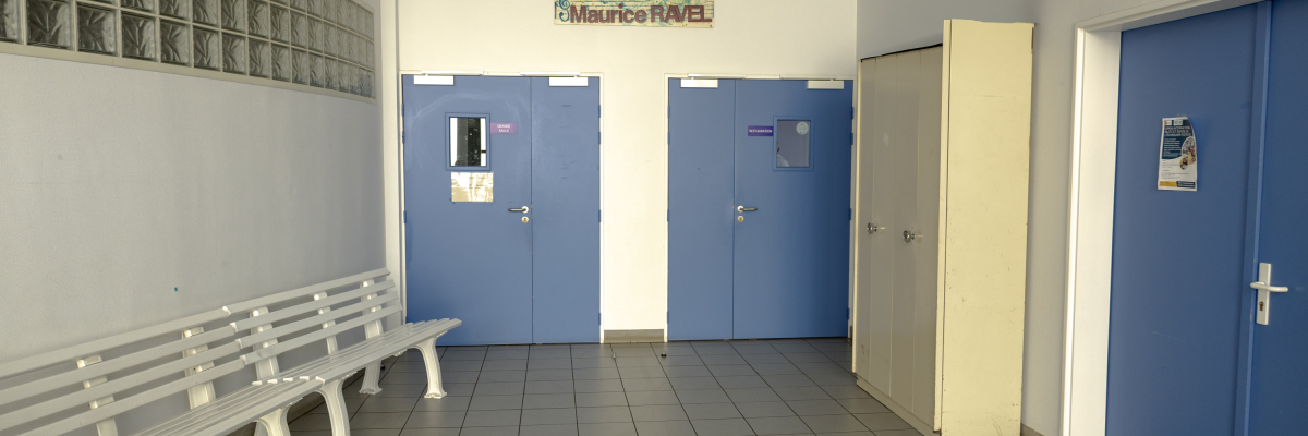Couloir avec banc, portes bleues, porte jaune et enseigne "Salles Maurice RAVEL".