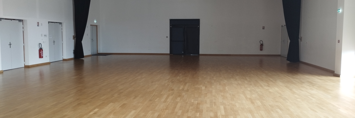 Salle vide avec parquet, éclairages suspendus, portes et extincteurs.