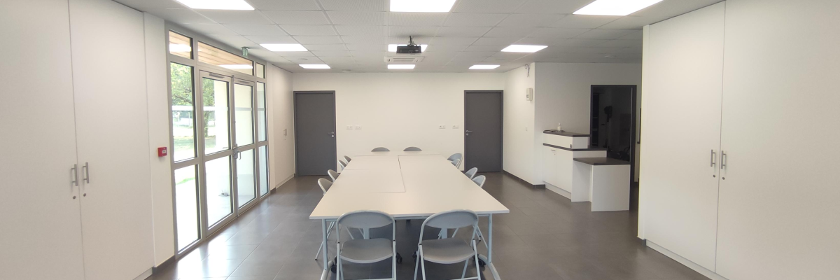 Salle de réunion avec table, chaises, vidéo projecteur, placards, portes et fenêtres.