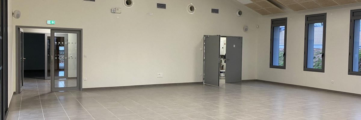 Salle vide avec portes, fenêtres, plafonnier et ventilation.