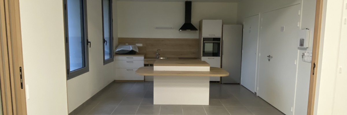 Cuisine avec îlot, hotte, placards et sol carrelé.