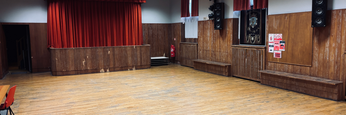 Salle avec scène, rideaux, bancs, haut-parleurs, affiches et porte.