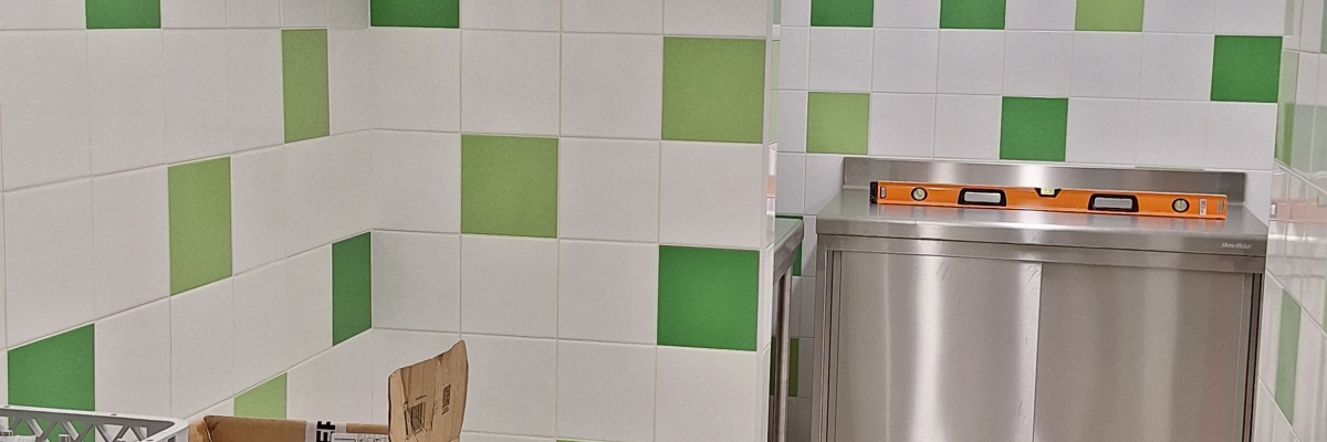 Cuisine avec plaques de cuisson, four, réfrigérateur, étagères et carrelage vert et blanc.