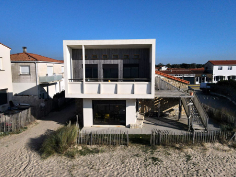 Maison moderne en bord de plage avec terrasse, escalier et clôture.
