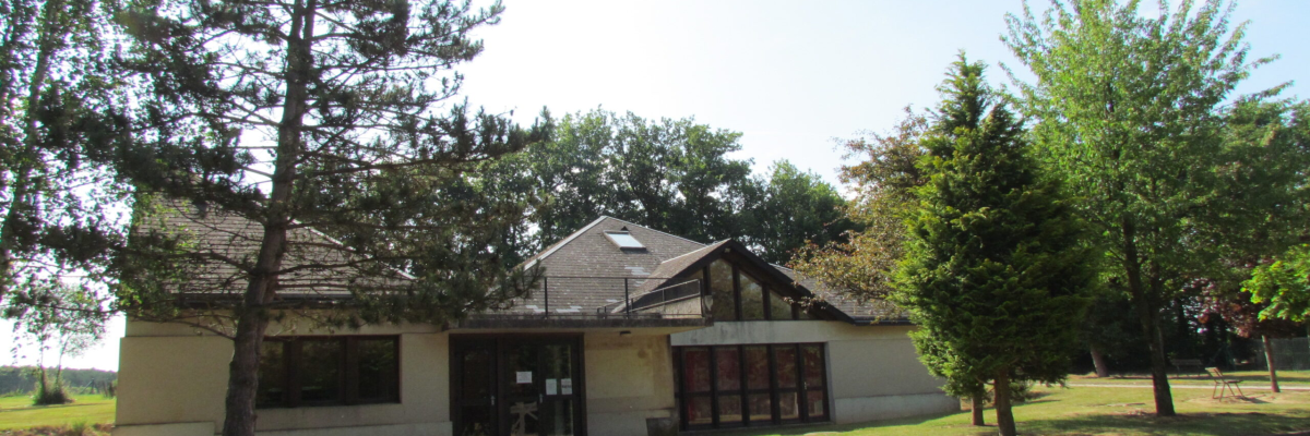 Bâtiment avec entrée, fenêtres, arbres, pelouse et parking.