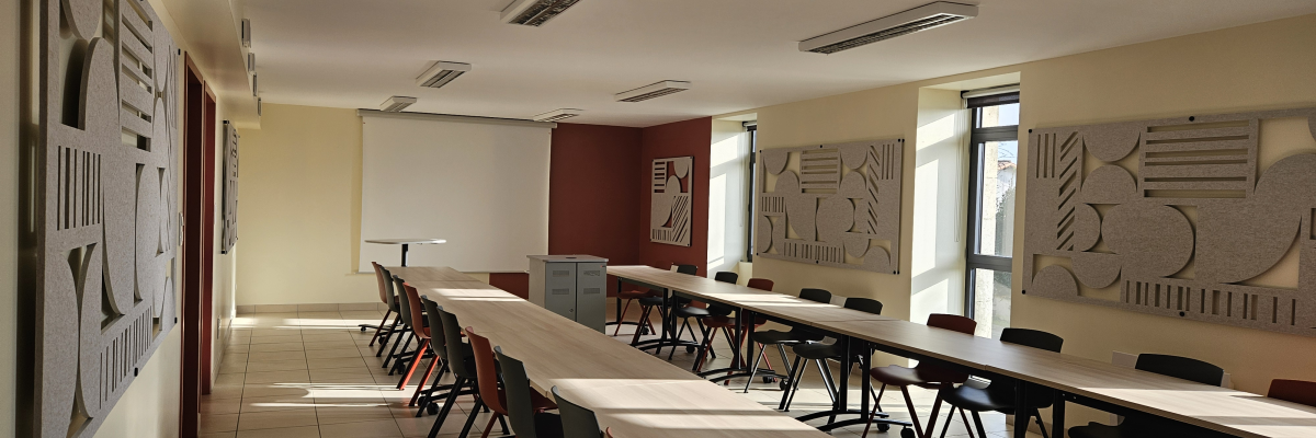 Salle de classe avec deux longues tables, chaises, tableaux et lumière naturelle.