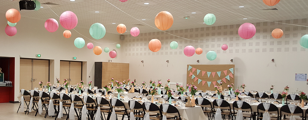 Salle avec tables, chaises, lanternes suspendues, fleurs et bannières.