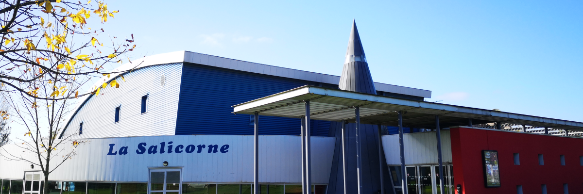 Un bâtiment industriel avec un panneau indiquant "La Salicorne", une pelouse verte et des arbres à feuilles caduques.