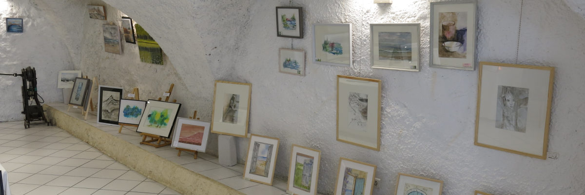 Galerie d'art avec tableaux encadrés alignés le long d'un mur blanc voûté.
Plafond blanc, sol carrelé.