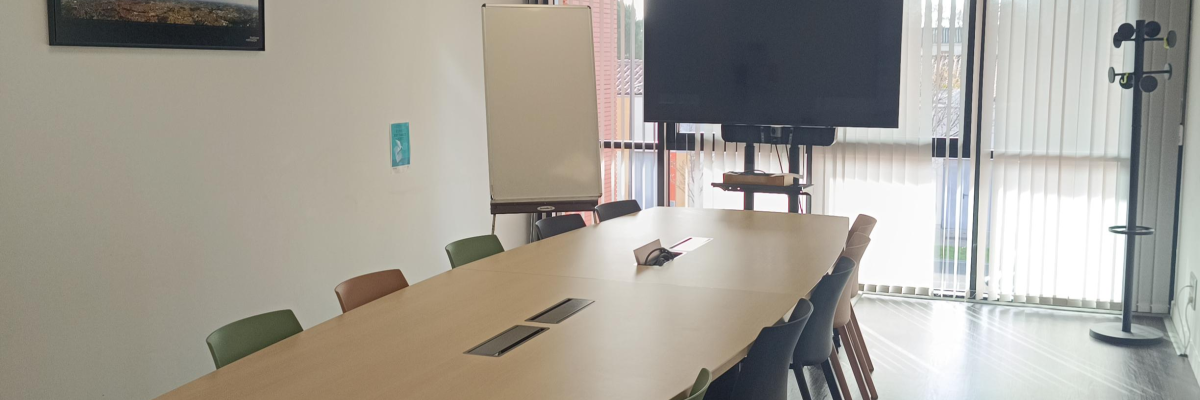 Salle avec table, chaises, écran et porte vitrée.