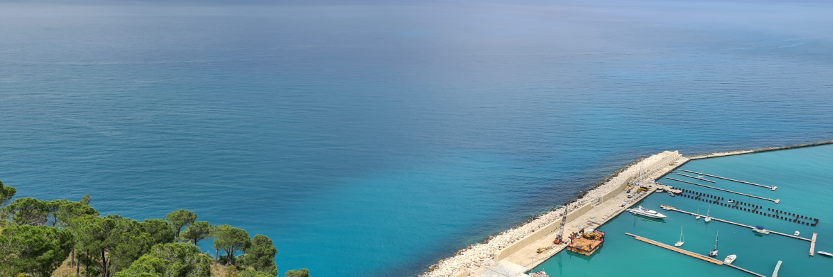 Vue sur mer avec plage, digue et port de plaisance.