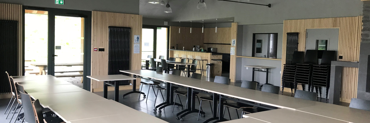 Salle avec tables, chaises, luminaires, cuisine, armoires et porte.