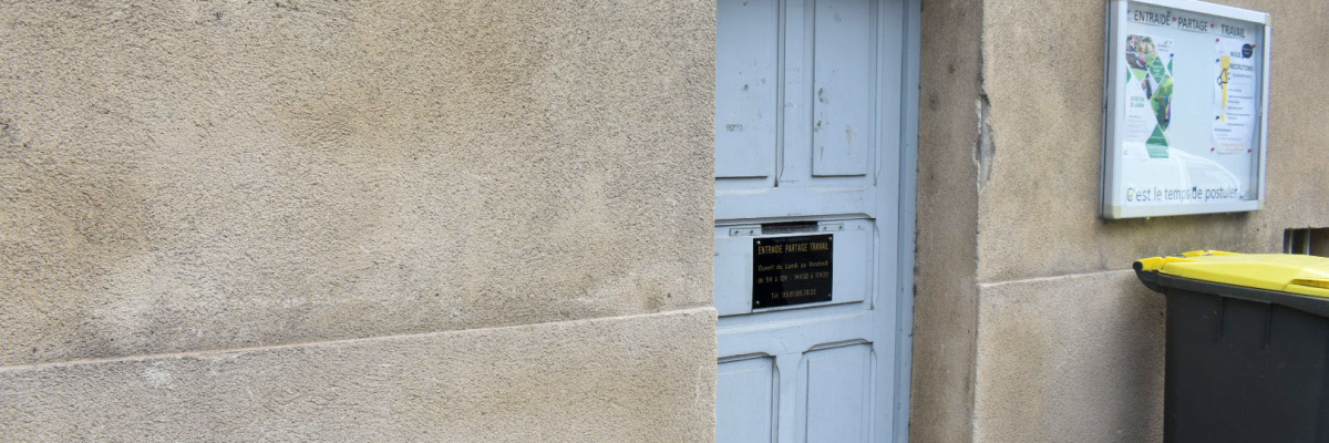 Maison avec porte bleue, plaque murale et poubelle.