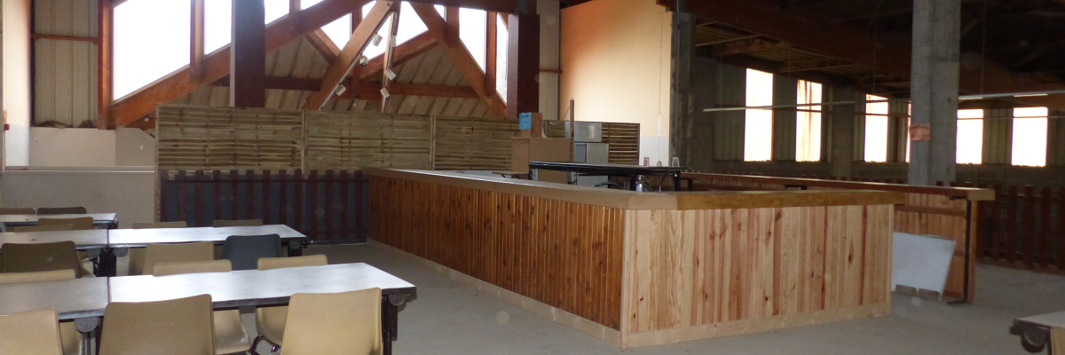 Salle avec tables, chaises, comptoir en bois, étagères et fenêtres.