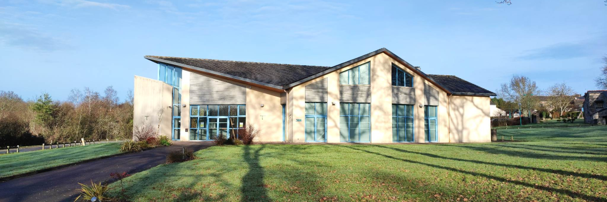 Bâtiment moderne avec grandes fenêtres, pelouse, arbre et ciel bleu.