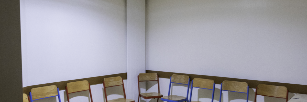 Salle avec rangée de chaises face à un mur blanc.