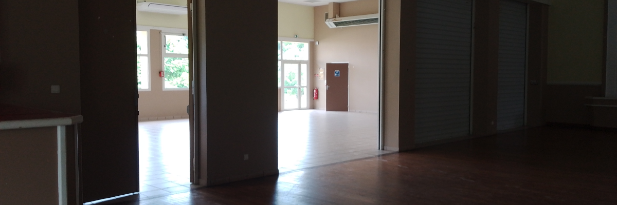 Salle vide avec portes ouvertes, plancher en bois, rampes, climatiseur mural.