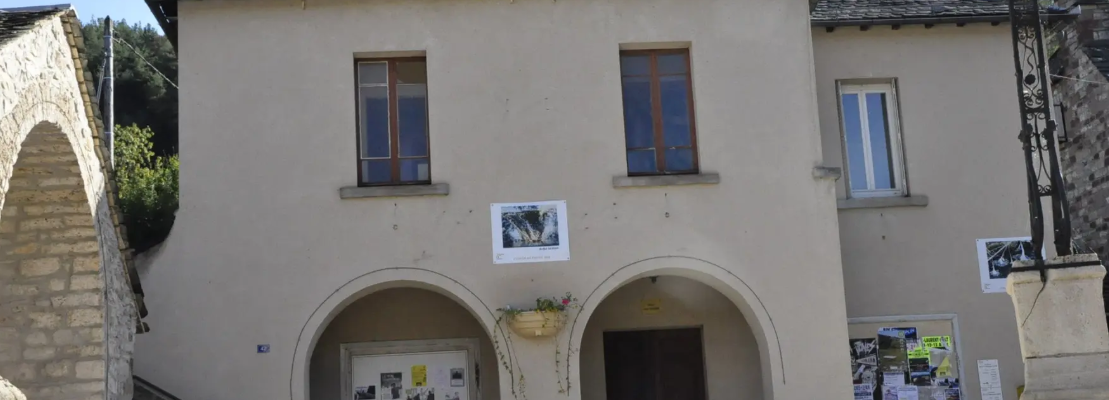 Bâtiment avec deux portes et deux fenêtres, affiches, plantes et antenne sur le toit.