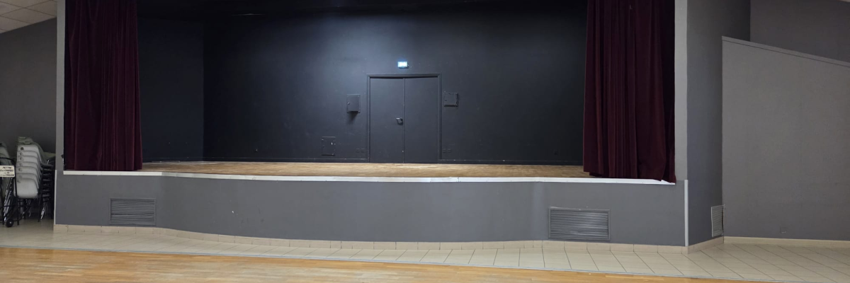 Salle avec scène, rideaux, porte, éclairages et parquet.