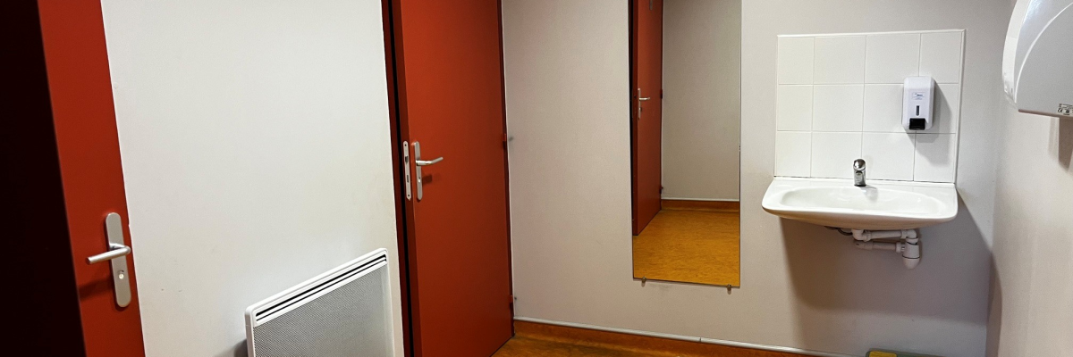 Toilettes avec porte rouge, lavabo, distributeur de savon, sèche-mains et radiateur.