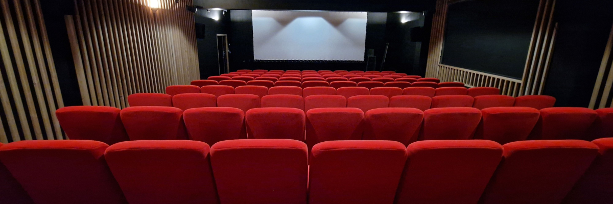 Salle de cinéma avec sièges rouges, écran et projecteur.