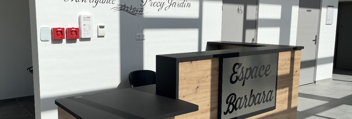 Réception avec bureau en bois, écrans, clavier, souris, et inscriptions murales.