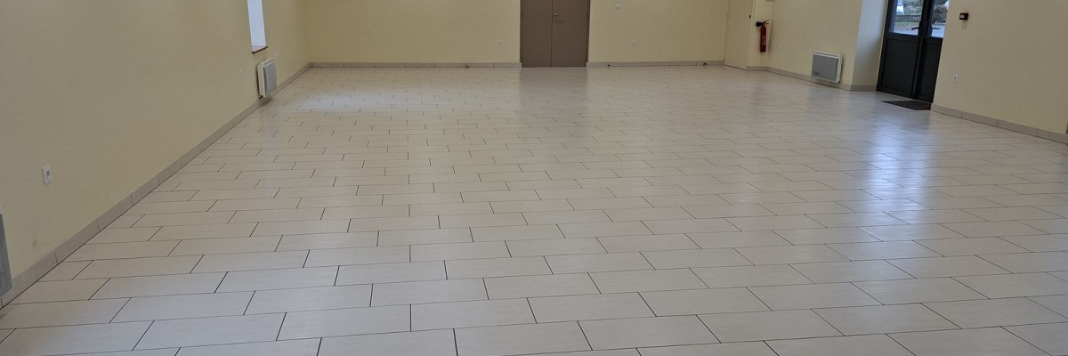 Salle vide avec sol carrelé, portes, ventilations murales et plafonnier.