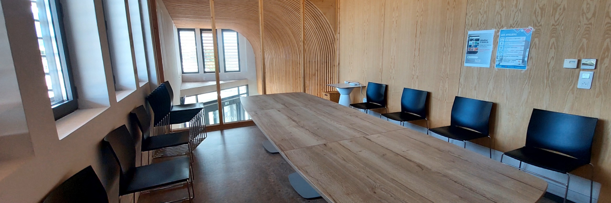Salle de réunion avec grande table, chaises, tableau d'affichage et fenêtres.