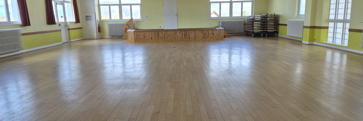 Salle spacieuse avec parquet, tables empilées, tableau blanc et grand miroir.