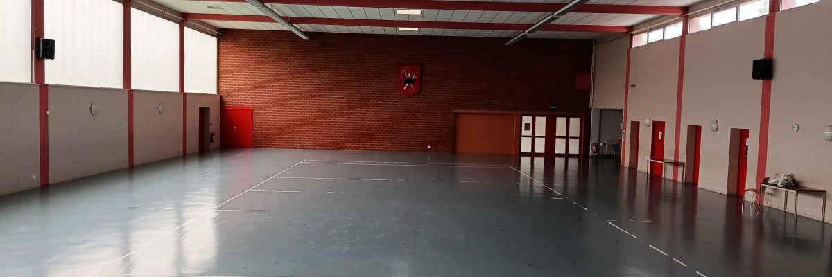 Salle spacieuse avec sol noir, murs rouges et blancs, portes, fenêtres et quelques équipements sportifs.