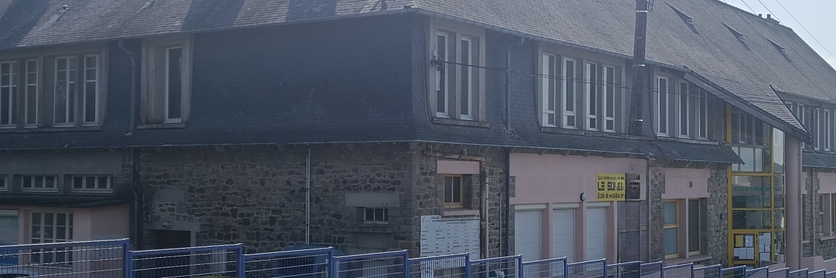 Bâtiment avec toit en ardoise, murs en pierre et enduit, fenêtres et portes, clôture métallique.