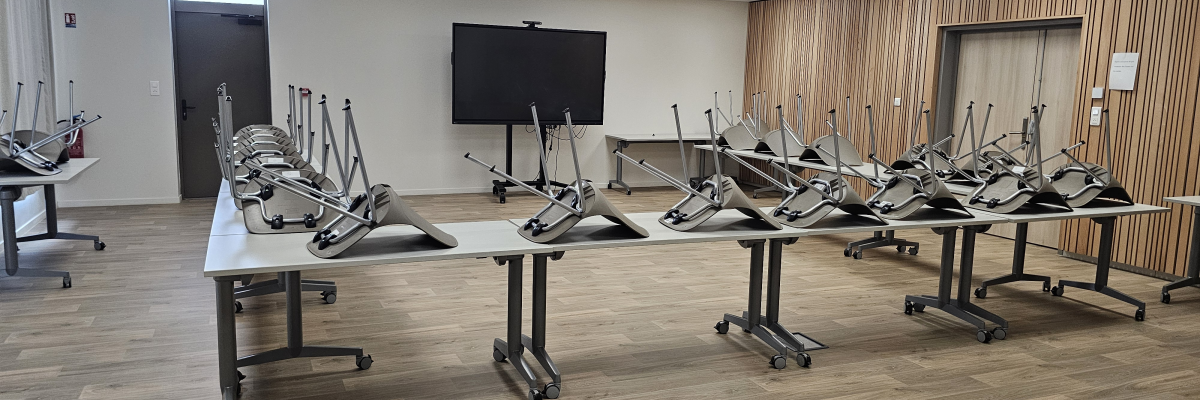 Salle avec tables, chaises et écran.