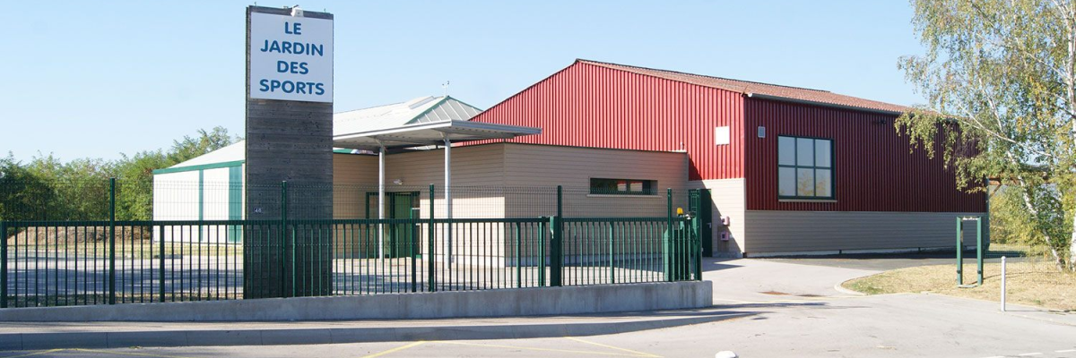 Bâtiment avec panneau "Le Jardin des Sports", clôture, route, et arbre.