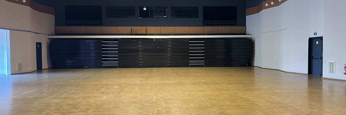 Salle spacieuse avec plancher en bois, rangées de chaises et murs blancs et bleus.