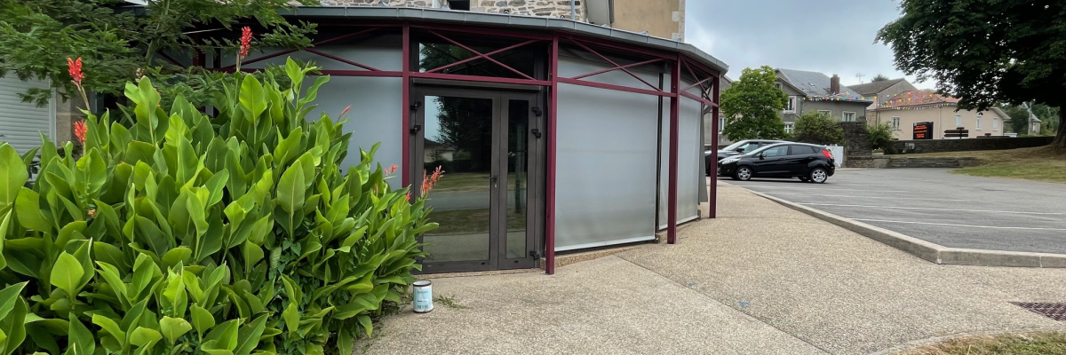 Bâtiment avec extension moderne, allée goudronnée, voiture et buissons.