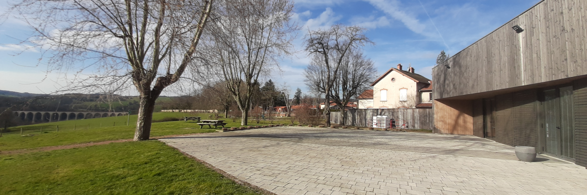 Parking avec allée pavée, arbres, bâtiment, ciel bleu et montagnes au loin.