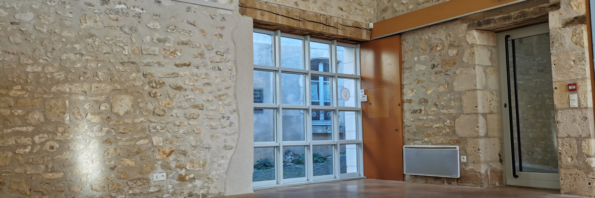 Salle avec mur en pierre, table, portes vitrées, radiateur, électricité, sortie de secours.