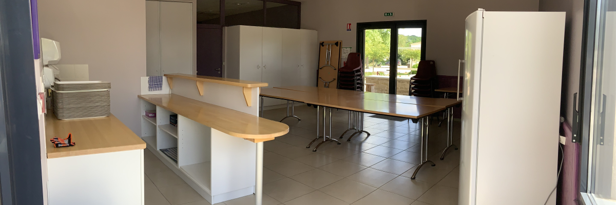 Salle avec tables, chaises, armoires, porte, fenêtre, frigo, évier, poubelle.