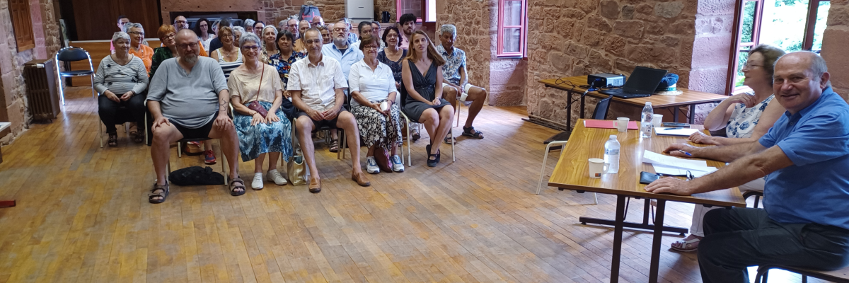 Salle avec parquet, murs en pierre, chaises, tables, projecteur et rideau.