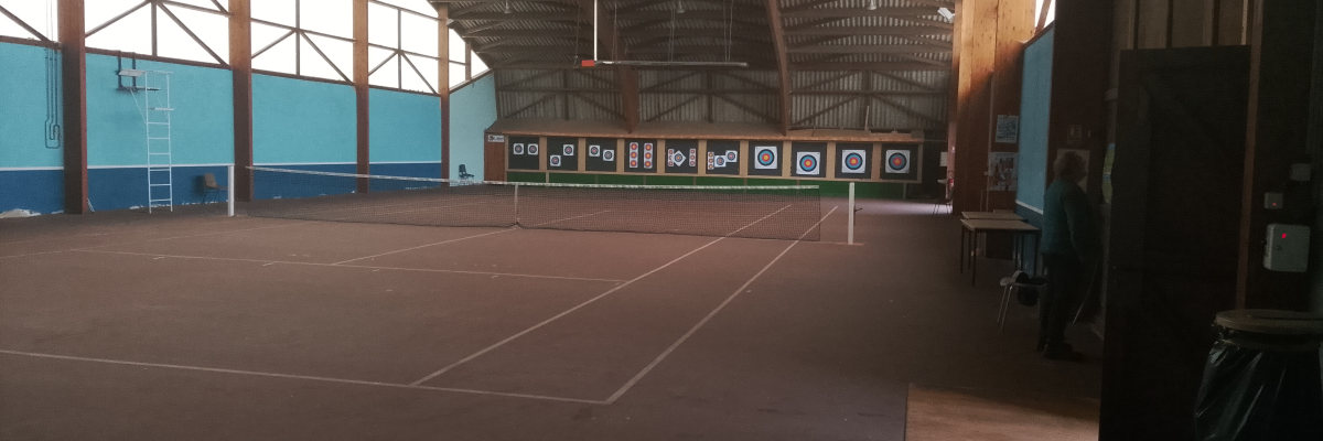 Salle intérieure avec terrain de tennis, cibles de tir à l'arc, table et chaises.