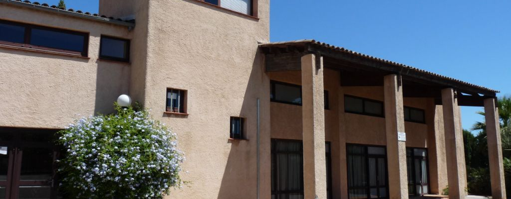 Bâtiment moderne avec toits plats, colonnes et fenêtres. Arbre et réverbère devant.
